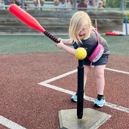 young girl with big smile hitting baseball off tee
