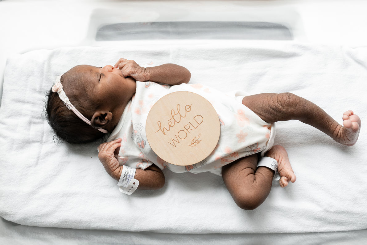 Newborn baby sleeping in a hospital bassinet with the sign "Hello World" during a Fresh 48 photo session in Moncton NB.