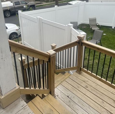 Wooden deck stairs with black railing leading to backyard