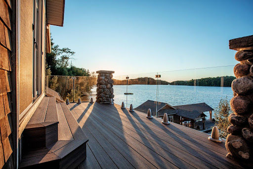 Lakefront deck made from composite decking with glass railing and stone pillars.