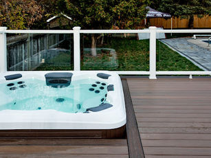 an open hot tub with a surrounding composite deck and glass railing.