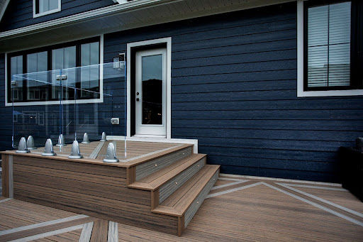 Deck stair platform against a blue house with glass railing.