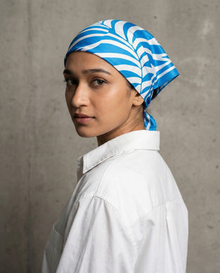 Woman wears blue and white satin scarf as head wrap