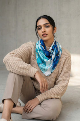 A woman wears a blue and gold abstract marble print satin scarf styled in a front bandana drape.