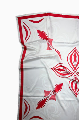 A close-up of a white satin scarf with a red abstract pattern and red border.