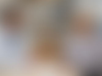 A doctor in a white coat with a stethoscope around their neck sits at a desk, speaking with a patient in a floral-patterned shirt. The setting is a medical office with shelves of medicine bottles and files in the background.