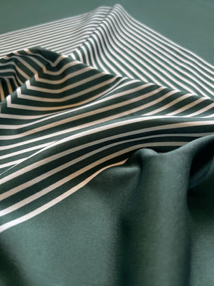 Close-up of draped green satin fabric showing a geometric white striped pattern.