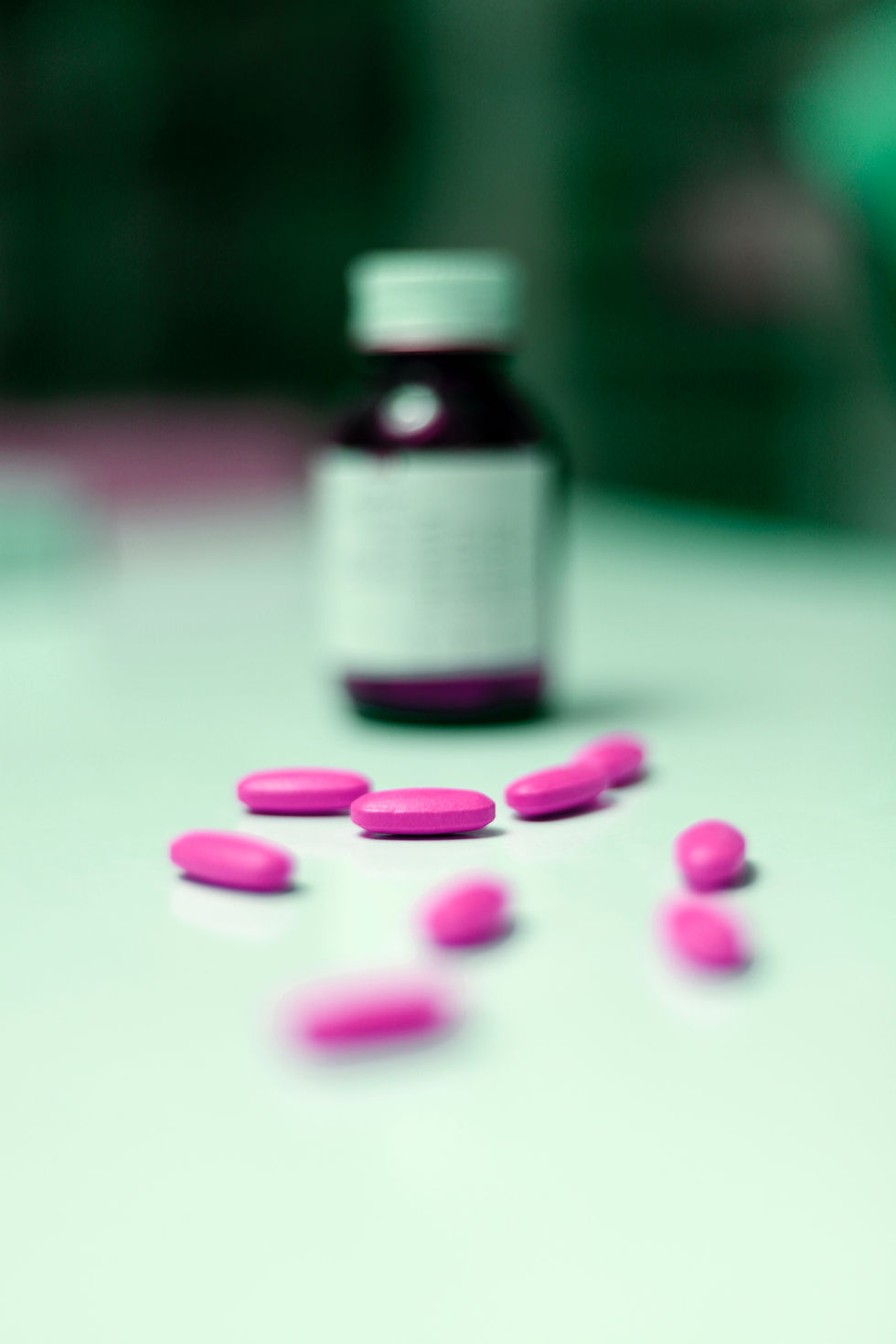 Bottle of medicine out of focus in the background, multiple pink pills in the foreground in focus. 