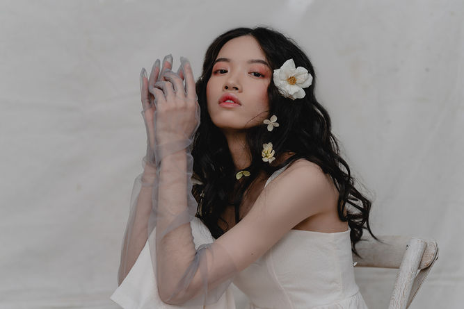 woman sitting before a light backdrop in a chair with flowers in her hair. 