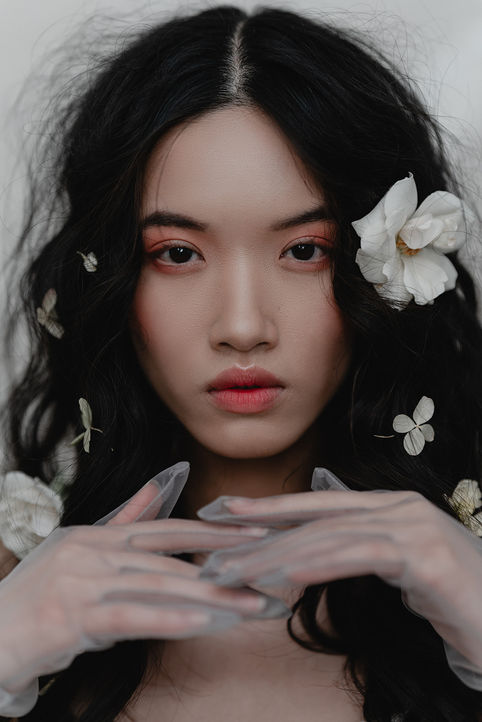 woman sitting before a light backdrop in a chair with flowers in her hair. 