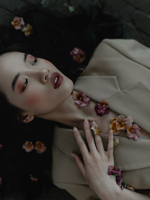 
woman laying on a dark floor in a blazer with pansies on her chest and in her hair. 