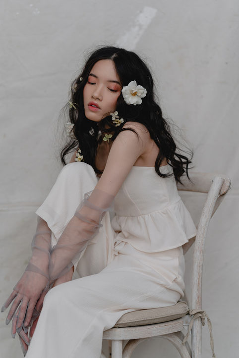 woman sitting before a light backdrop in a chair with flowers in her hair. 