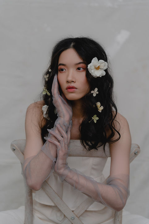 woman sitting before a light backdrop in a chair with flowers in her hair. 