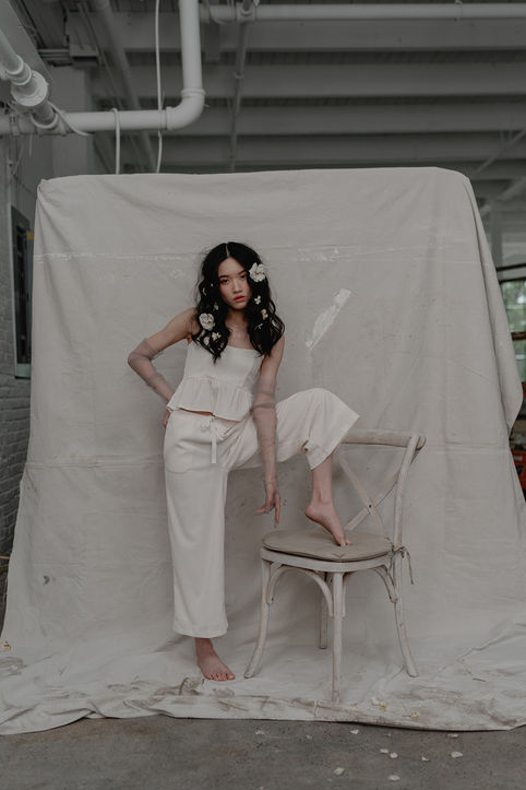 woman sitting before a light backdrop in a chair with flowers in her hair. 