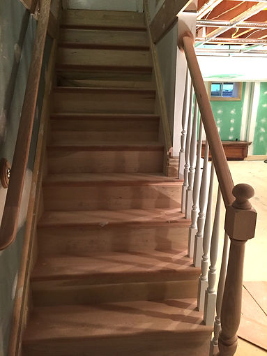 Image of a bare wood stairs and banaster in basement before staining