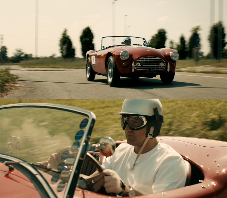 A man in a vintage racing helmet and goggles driving a red classic sports car