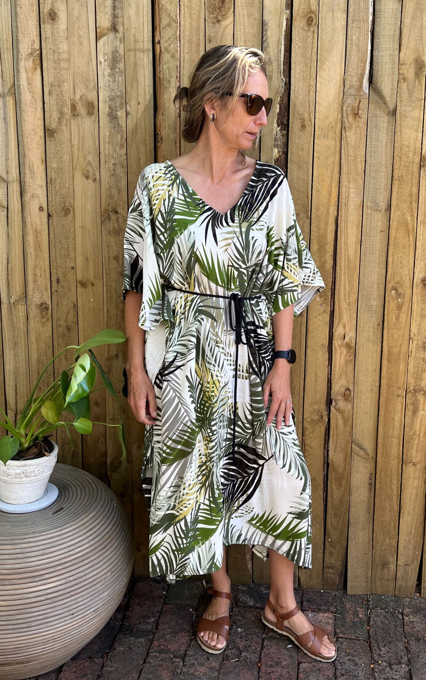 Woman wearing classic kaftan style with leaf print and tie belt. Made in rayon which is a natural breathable fabric.