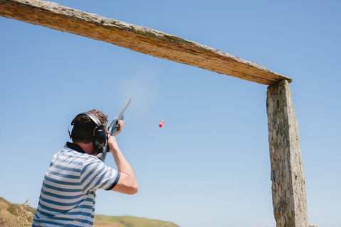 Man shooting a shotgun at red clay pigeon during event.