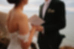 Couple exchanging vows, paper says 'vows', with ocean backdrop wedding ceremony.
