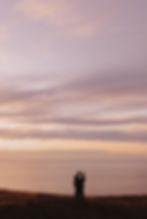 Couple silhouetted, watching beautiful sunset over ocean.