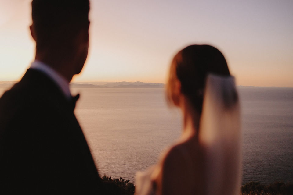 Couple looking at sunset over ocean, romantic wedding scene.