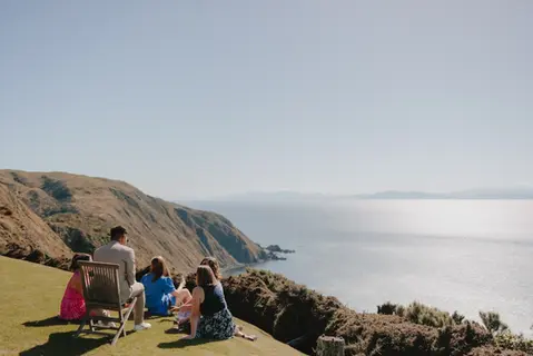Family group enjoying scenic ocean view from a grassy clifftop.