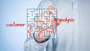 Person writing and connecting the two words "customer" and "analysis" by drawing a line through a see through maze "