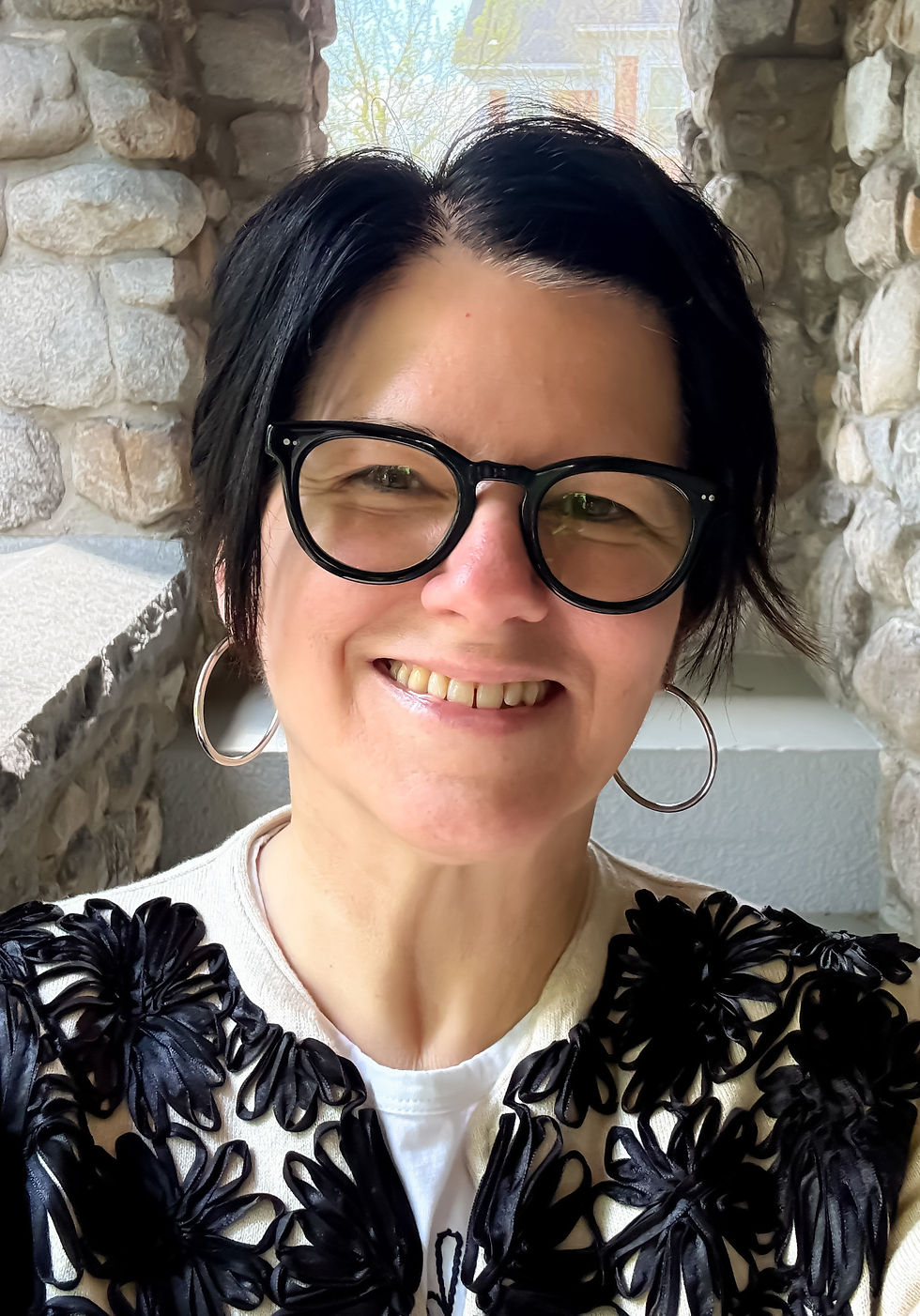 Stacy, founder of BEcoming Seen, smiling in glasses against a stone wall.