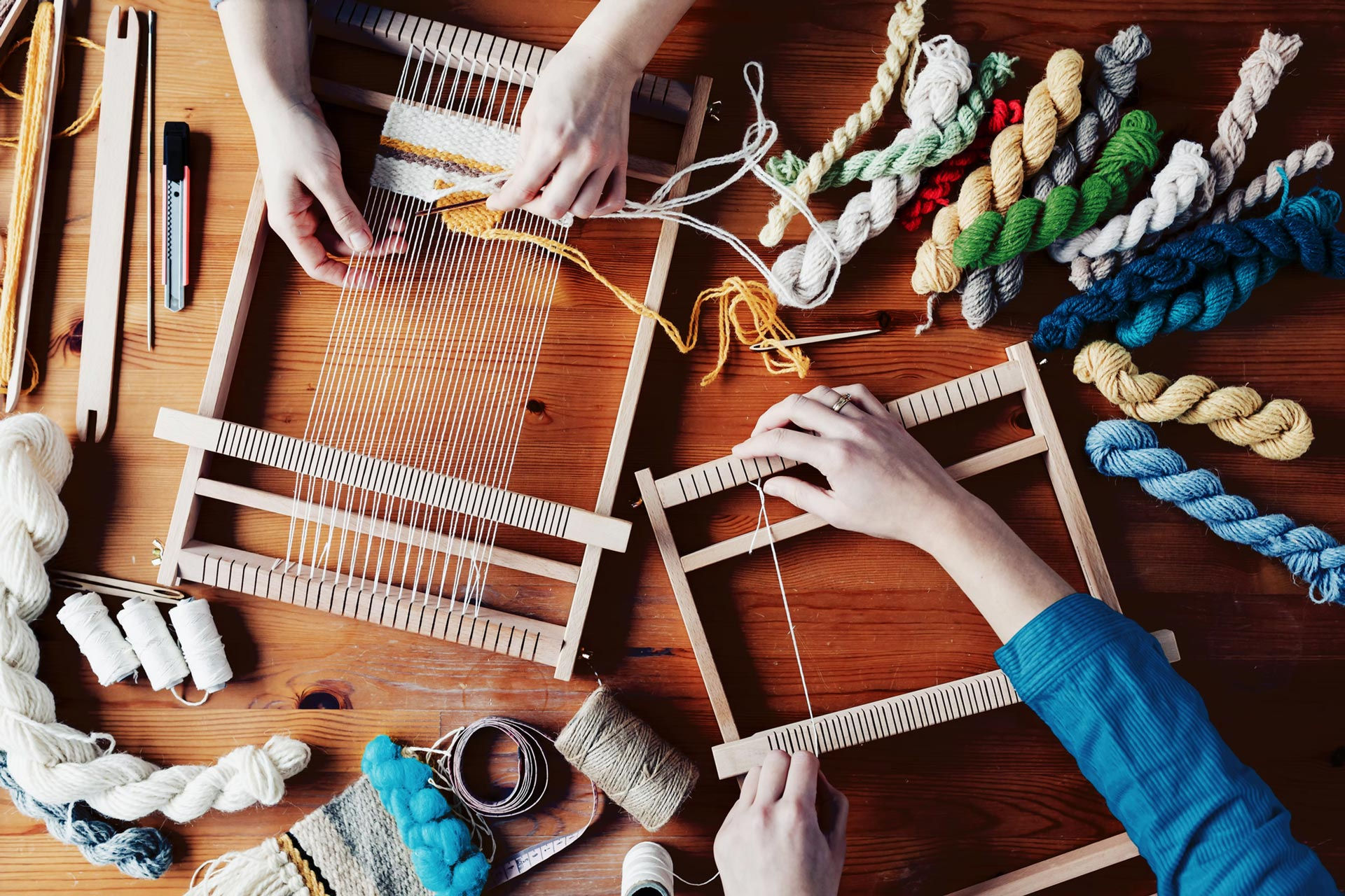 Two people weaving with colorful yarns on small wooden looms at a craft table