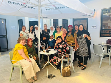 נשים מתחת לשמשיה מחייכות למצלמה חלקן יושבות וחלקן עומדות