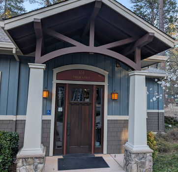 Entrance to building with wooden door, porch, and lights on the wall.