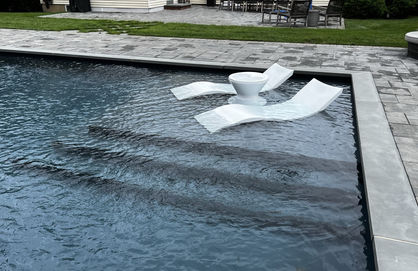 Swimming pool with two white floating lounge chairs and a small table