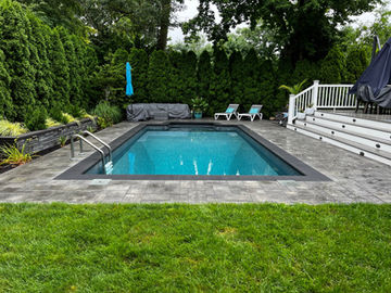 Rectangular pool with steps and handrails, surrounded by a patio