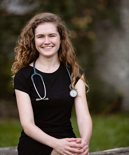 A portrait of Emma Ritchie - Life and Wellness Coach wearing a stethoscope in front of a natural background