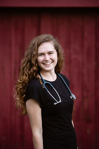 A portrait of Emma Ritchie - Life and Wellness Coach wearing a stethoscope in front of a red background