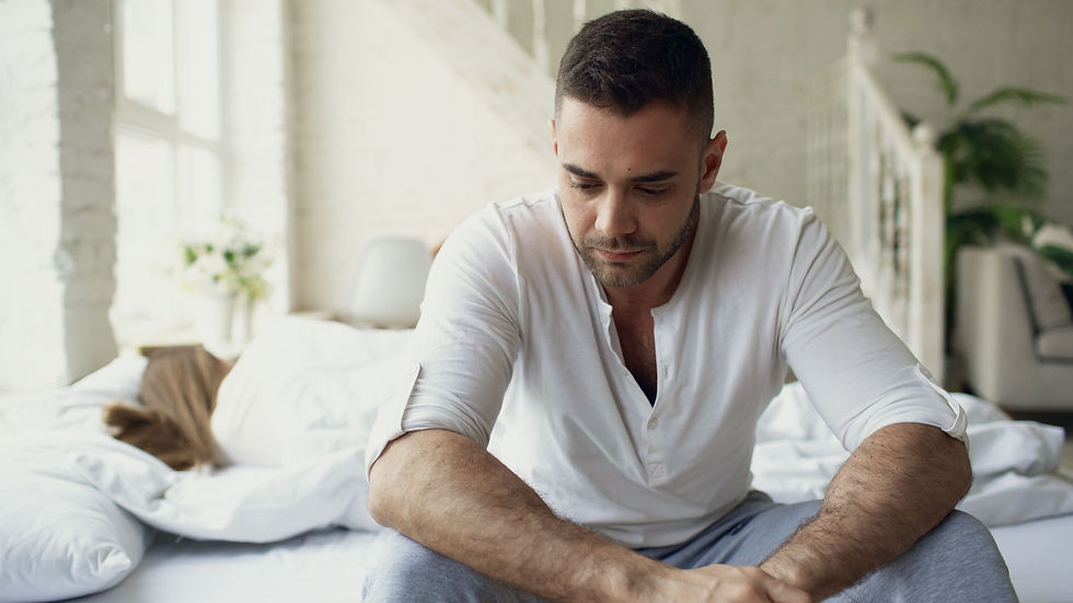 A frustrated and worried man sits up in bed as his wife sleeps beside him