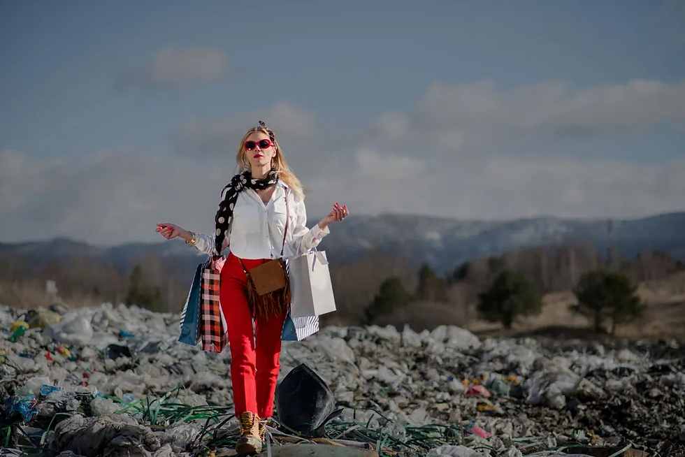 A woman dressed stylishly walks through a landfill, holding shopping bags amidst the discarded waste, highlighting a stark contrast between consumerism and environmental degradation.
