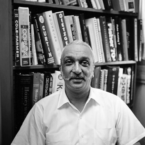 Grandpa Bill smiling warmly in front of a bookshelf filled with books.