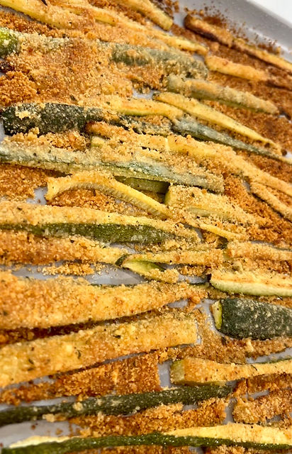 Close-up view of golden crispy baked zucchini fries on a white plate with marinara sauce