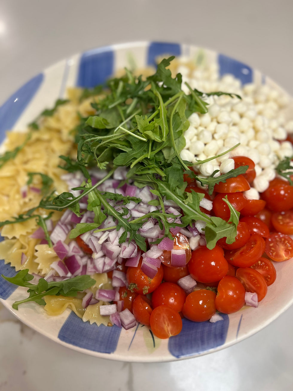 Eye-level view of a serving bowl with pesto pasta salad topped with fresh arugula and cherry tomatoes