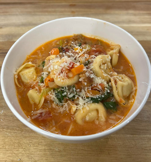 Eye-level view of a steaming bowl of creamy sausage and tortellini soup with fresh spinach