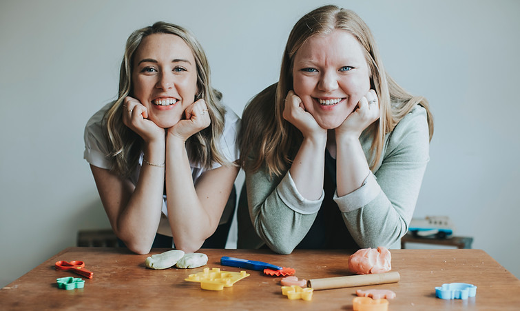 A photo of Jaelyn and Lindsey, with elbows propped on a table and chins resting on their hands.
