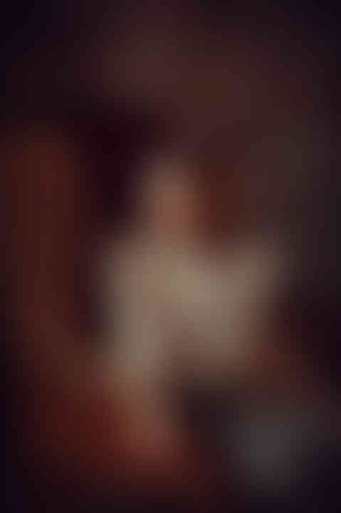 Girl in beige dress sitting on the brown chair in the dark studio