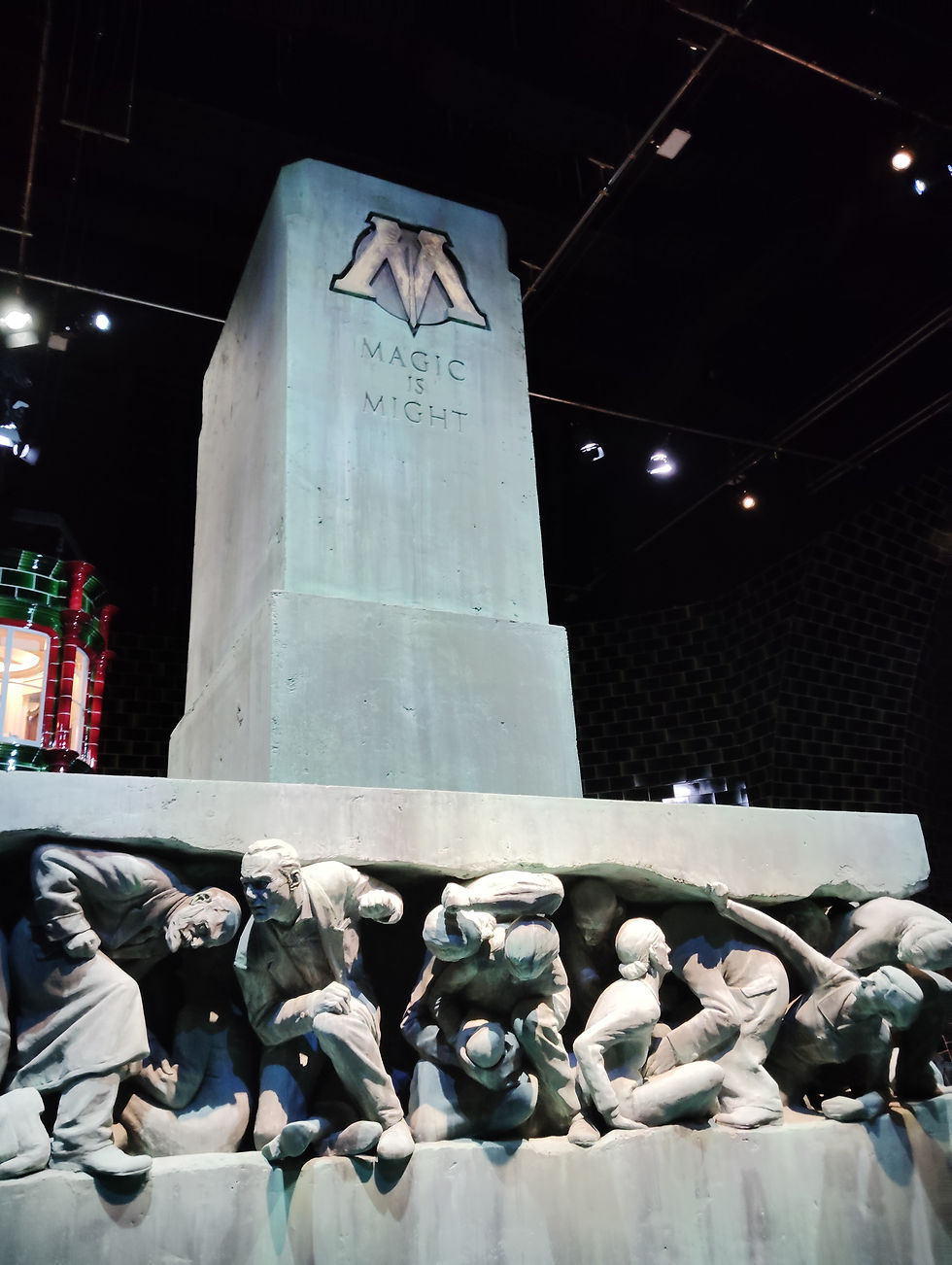 A tower on top of a concrete platform. On the tower is written "Magic is Might." Under the platform are statues of many people being crushed.