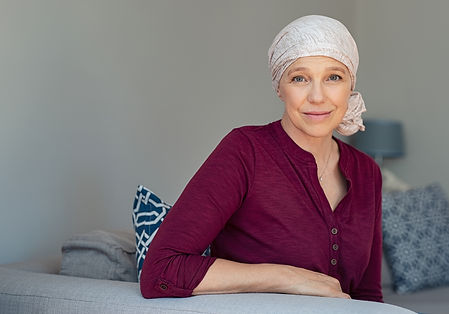 Mature woman with cancer in pink headscarf smiling sitting on couch at home. woman sufferi