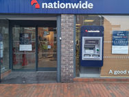 Nationwide bank entrance with an ATM beside it. Glass doors show "temporarily closed" sign. Brick and blue colour scheme. Wet pavement.