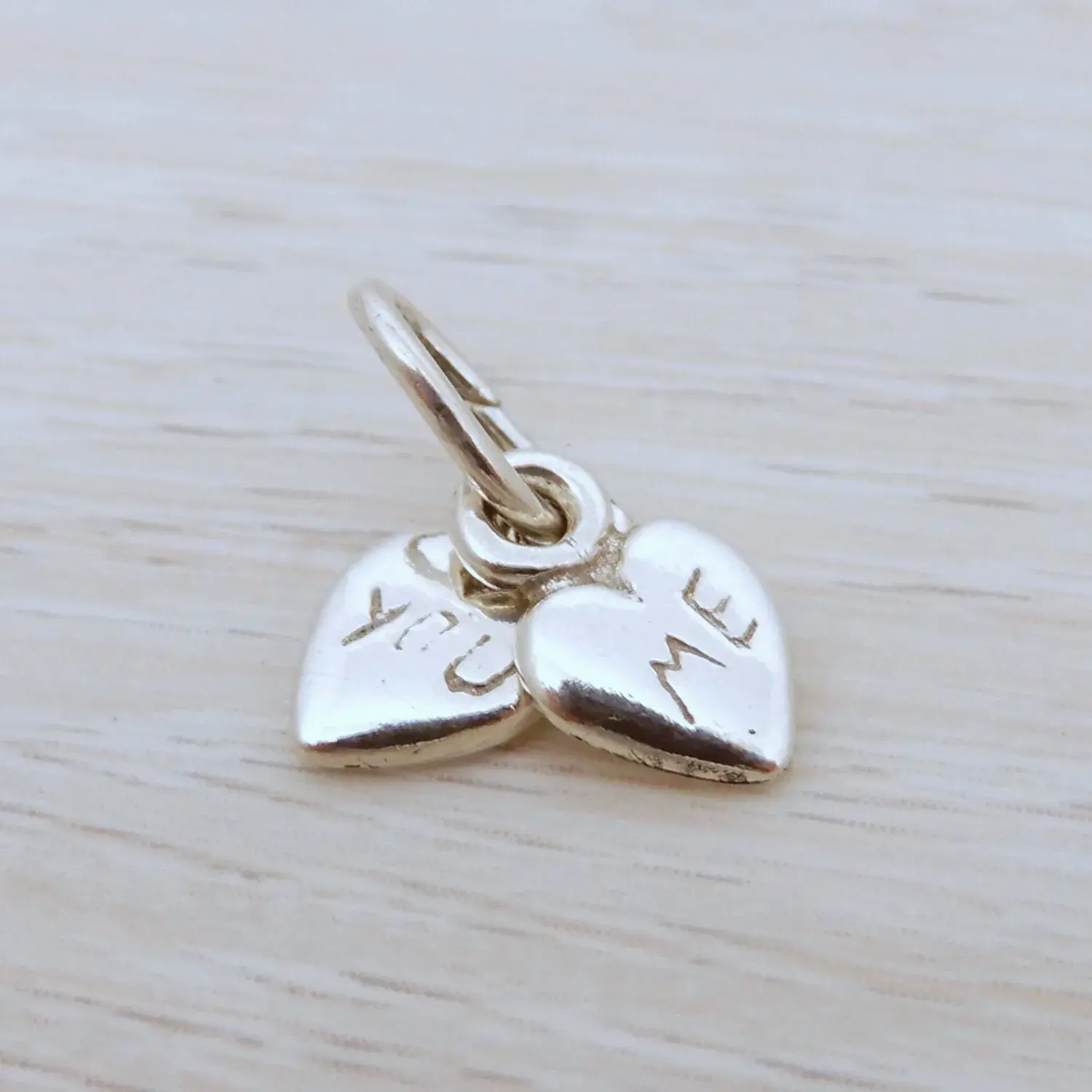Sterling silver ‘You and Me’ heart charm with engraved design on wood background