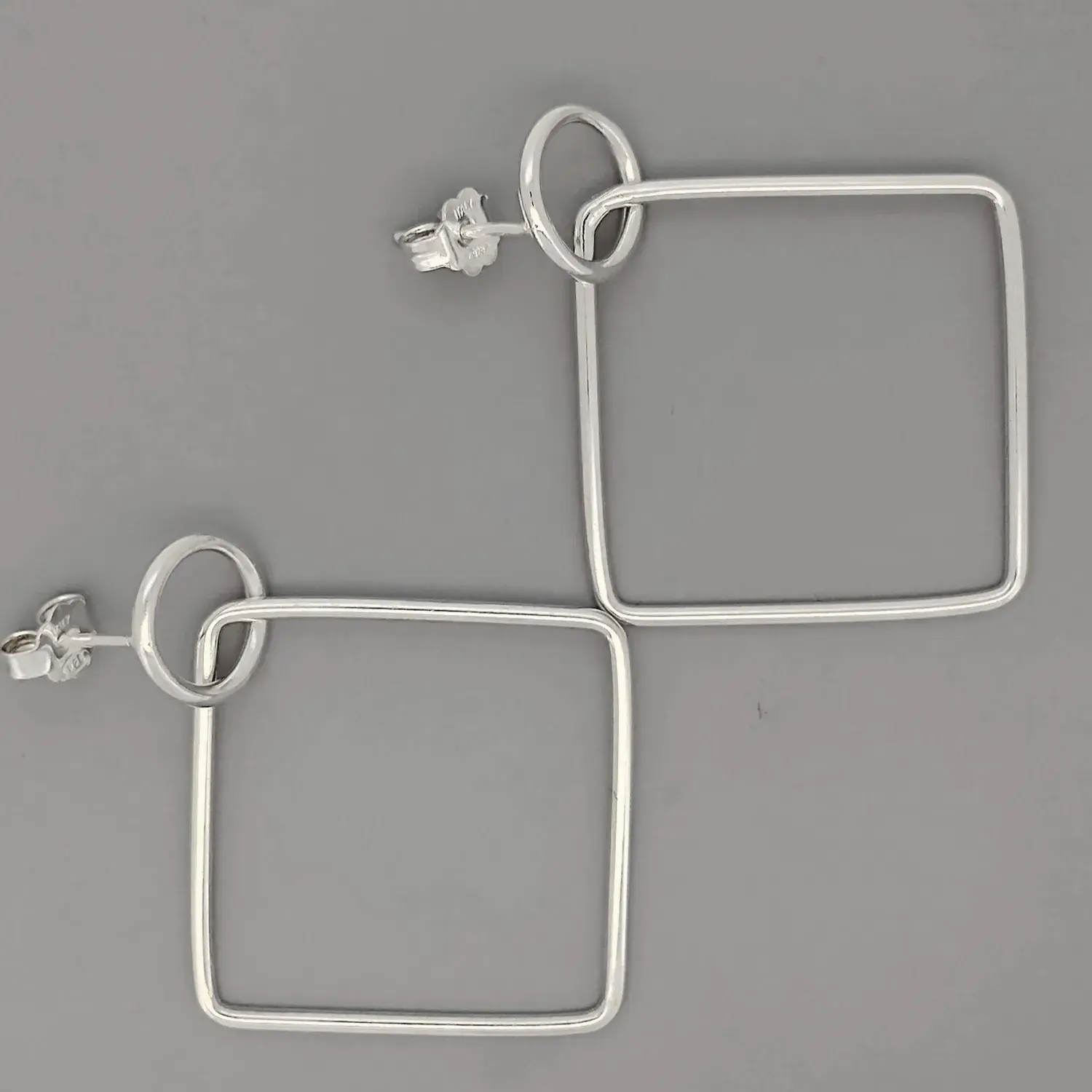 Close-up of sterling silver square drop earrings with polished finish, modern style.