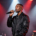 Man in black jacket singing into microphone on stage