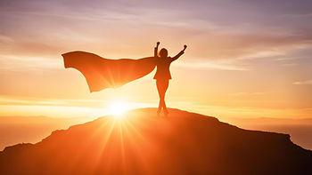 a woman standing on a hill with a cape flowing behind her with both arms in the air